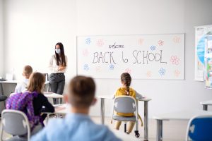 Teacher in elementary school room wearing a mask with social distancing students