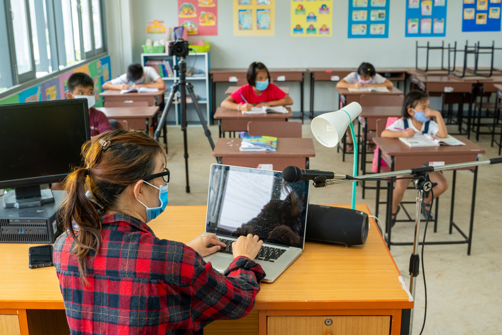 Teacher sitting at desk with laptop teaching class wearing masks